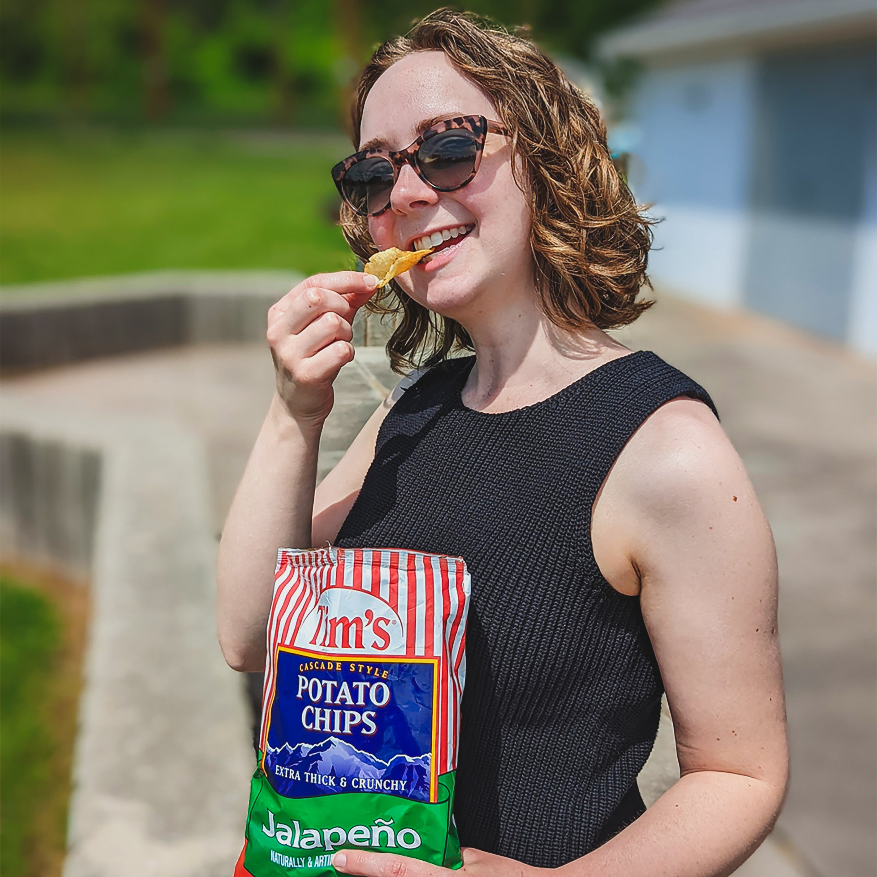Woman eating a chip from a bag of Tim's Jalapeno potato chips outdoors.