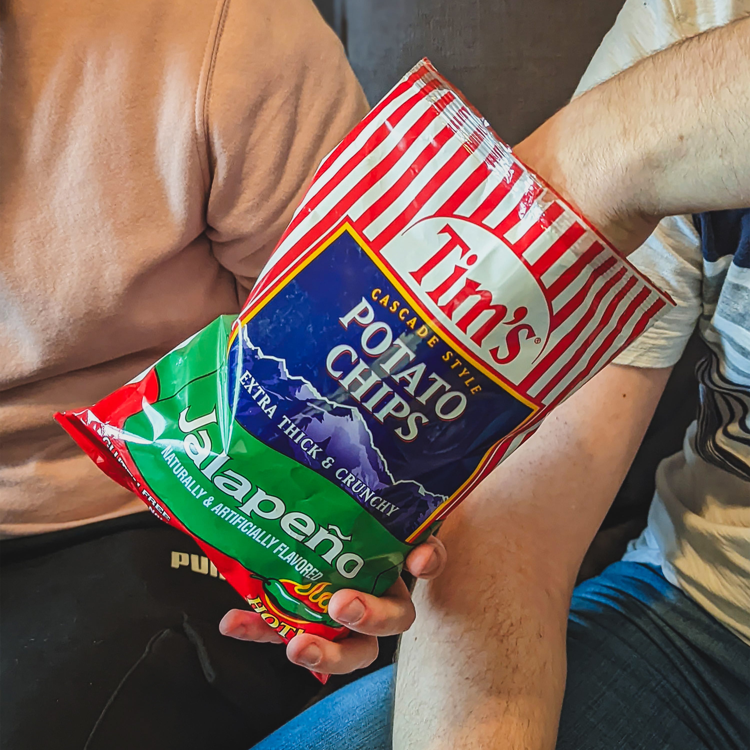 Person holding two bags of Tim's potato chips, one red and one green.