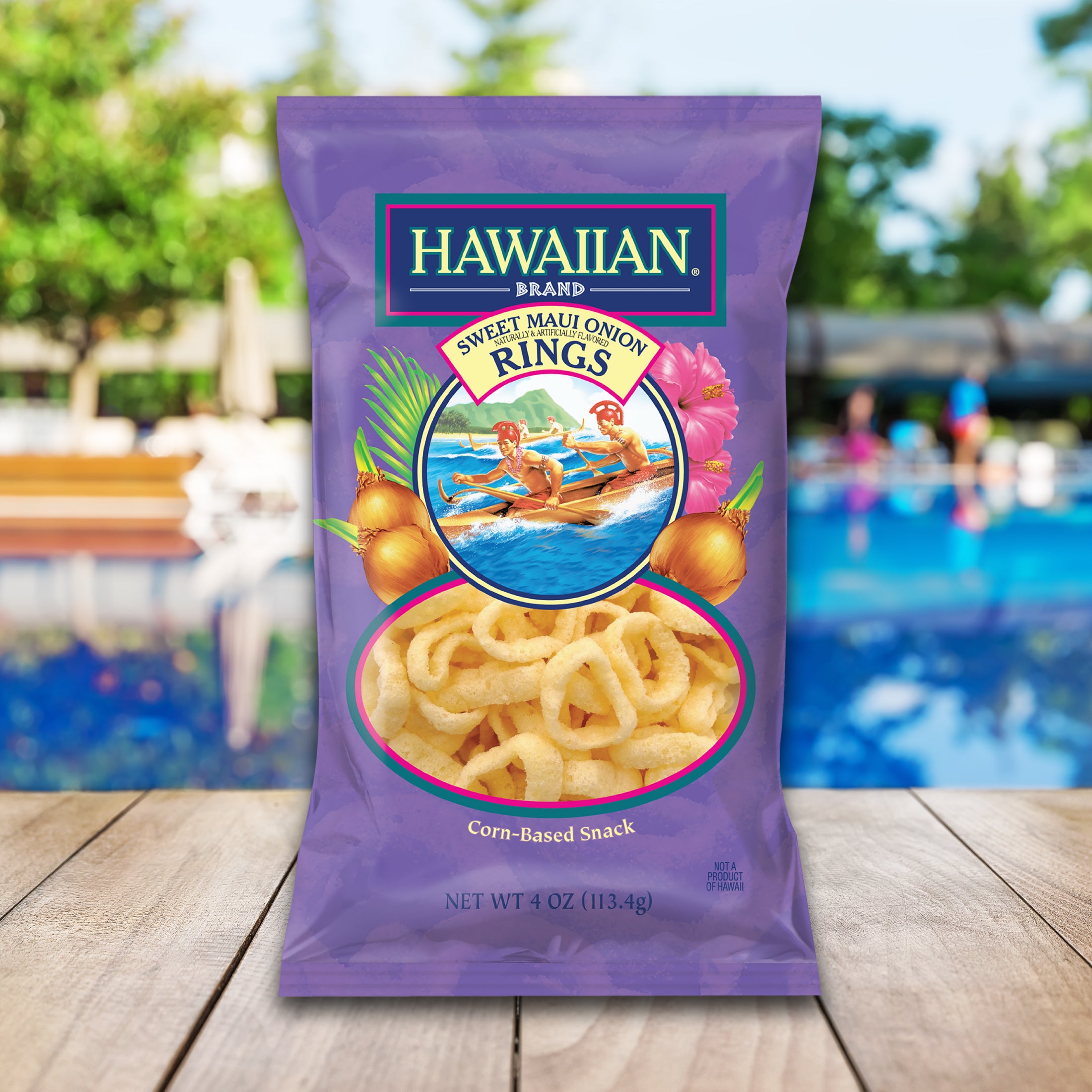 Hawaiian Brand Sweet Maui Onion Rings packaging on a wooden surface with a pool and beach chairs in the background.