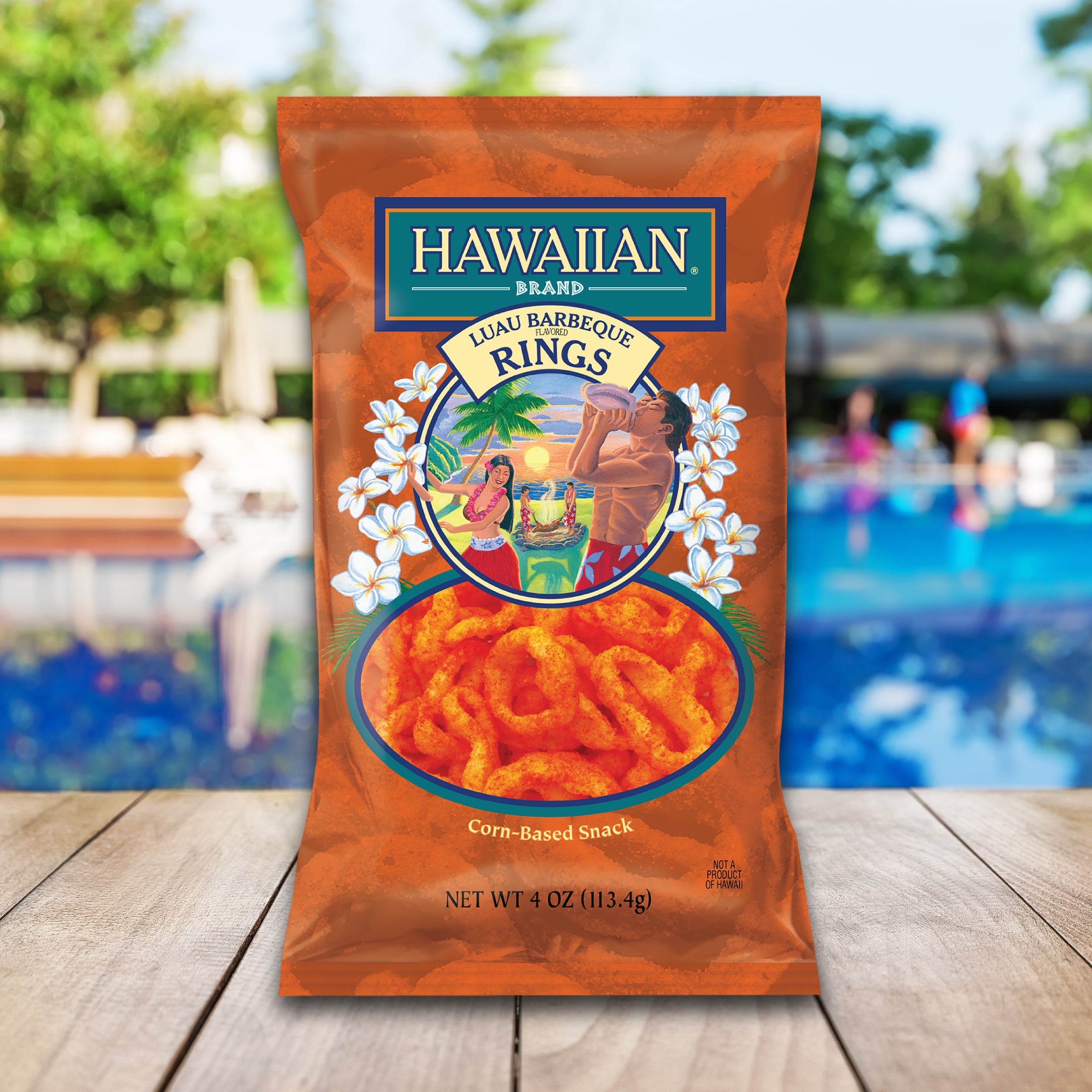 Hawaiian Brand Lava Barbecue Rings snack package on a wooden surface with a pool and beach chairs in the background.