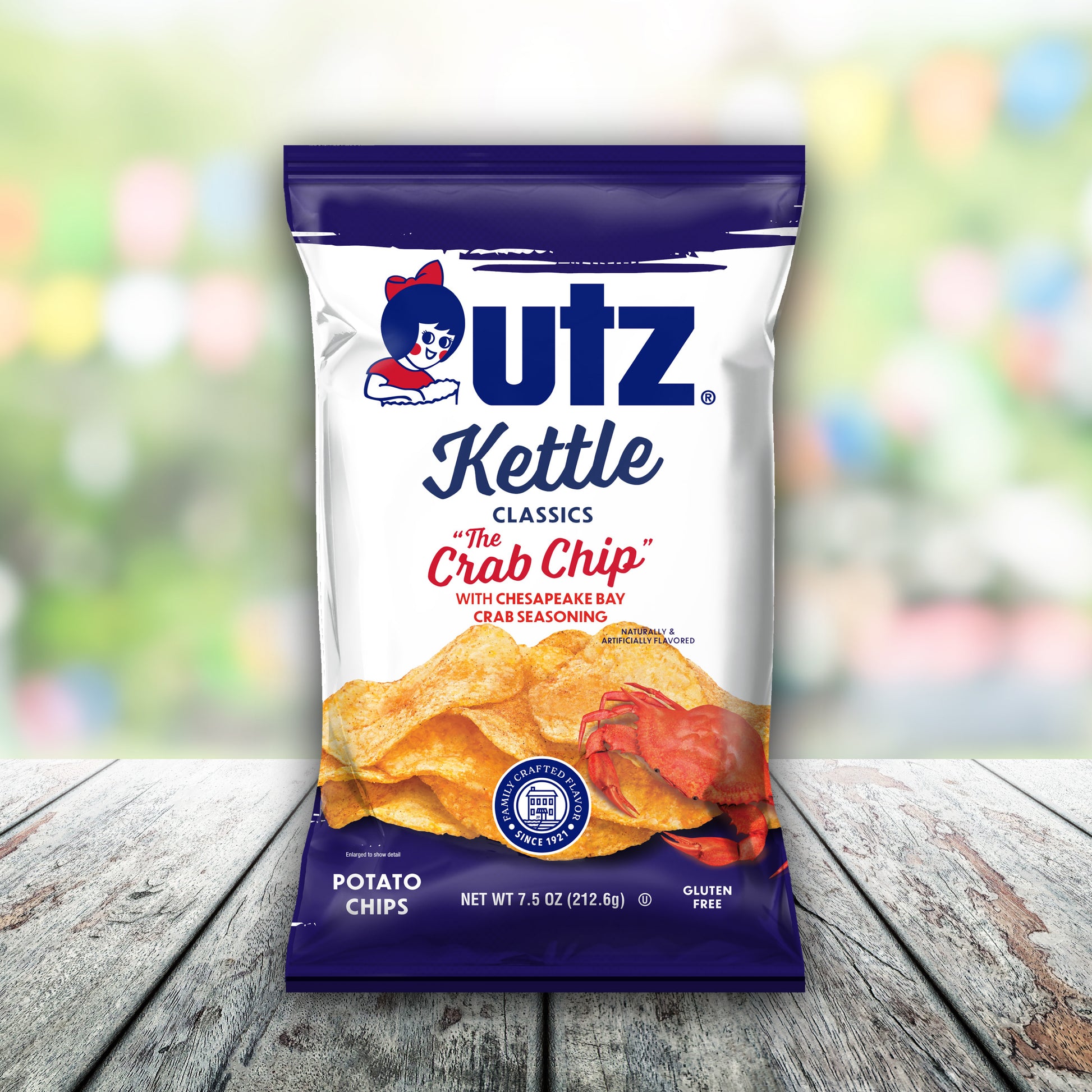 Outz Kettle Classics The Crab Chip potato chips packaging on a wooden surface with a blurred colorful background