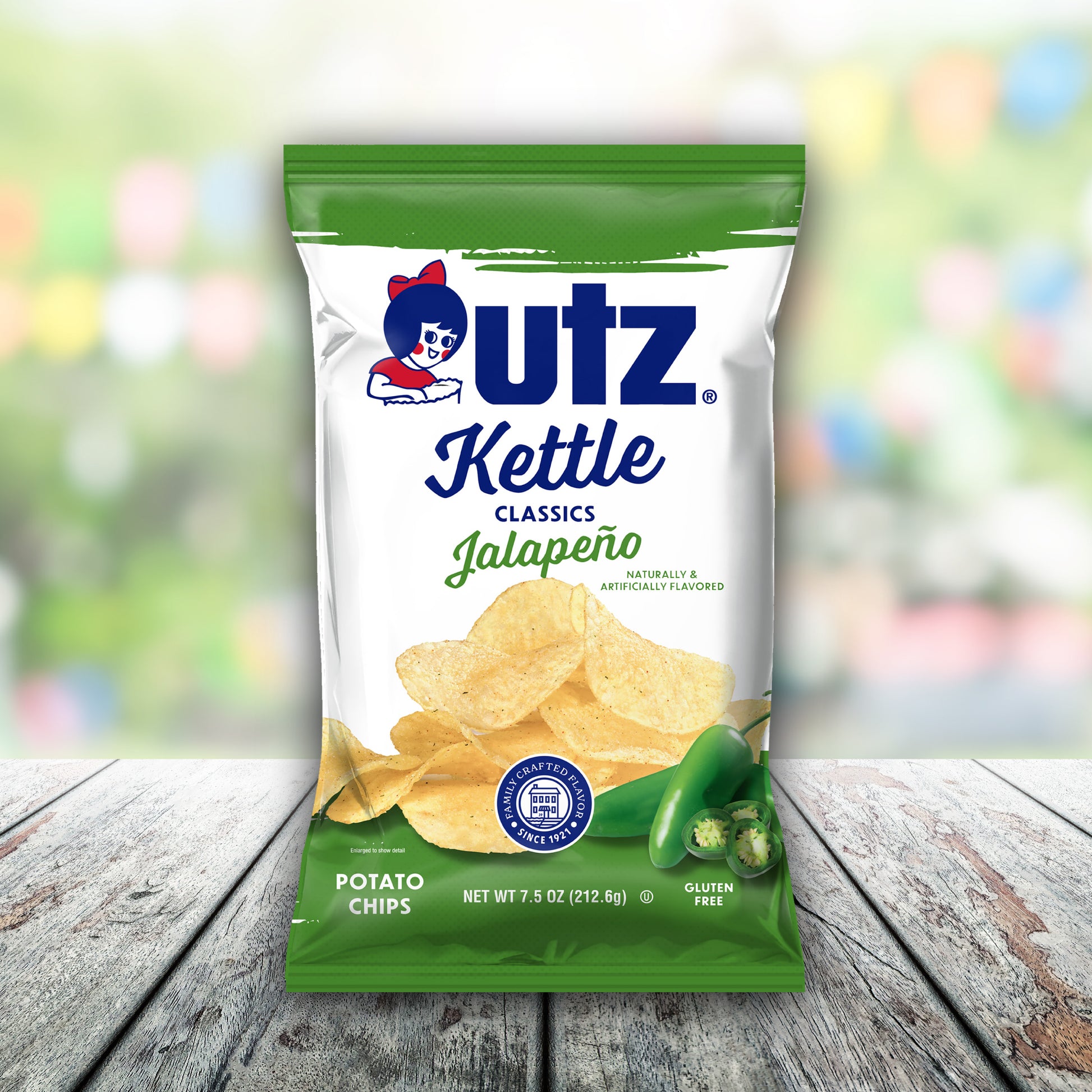 Outz Kettle Classics Jalapeno potato chips packaging on a wooden surface with a blurred colorful background