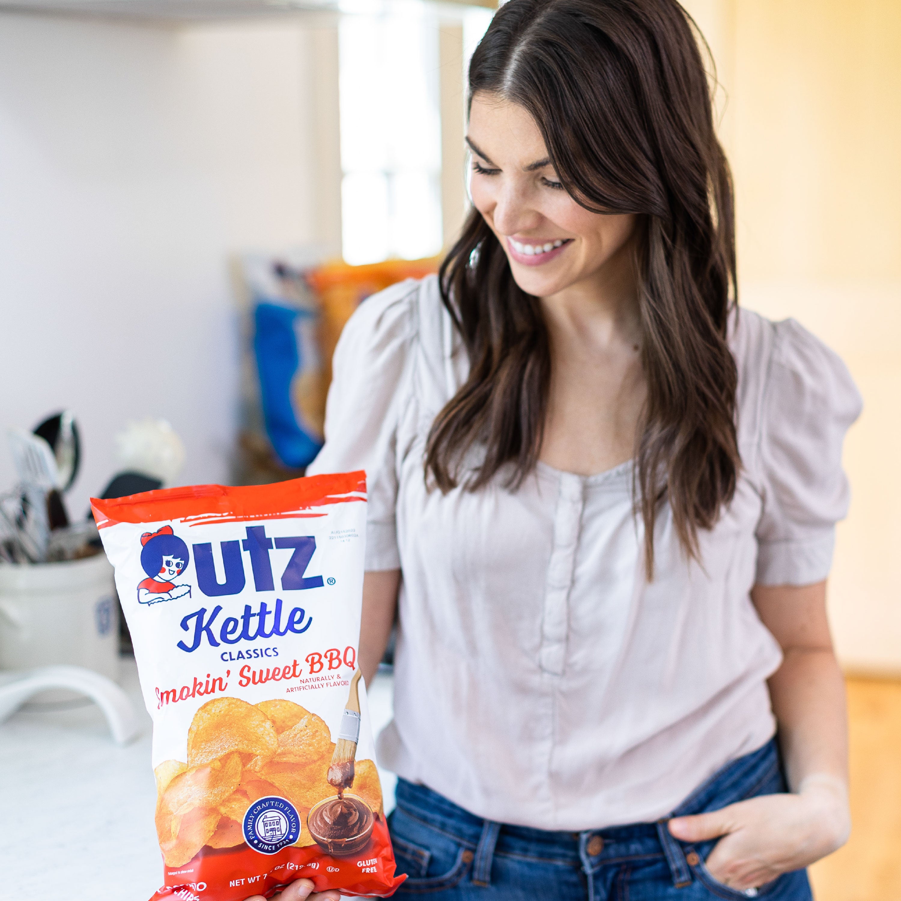 Woman holding a bag of Utz Kettle Classics makin' Sweet BBQ flavored chips in a casual setting.