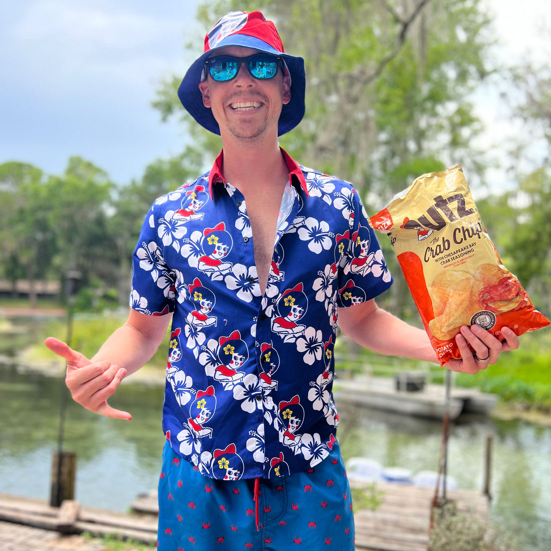 Man in a colorful shirt and hat holding a bag of Fritz's Crab Chips by a body of water.