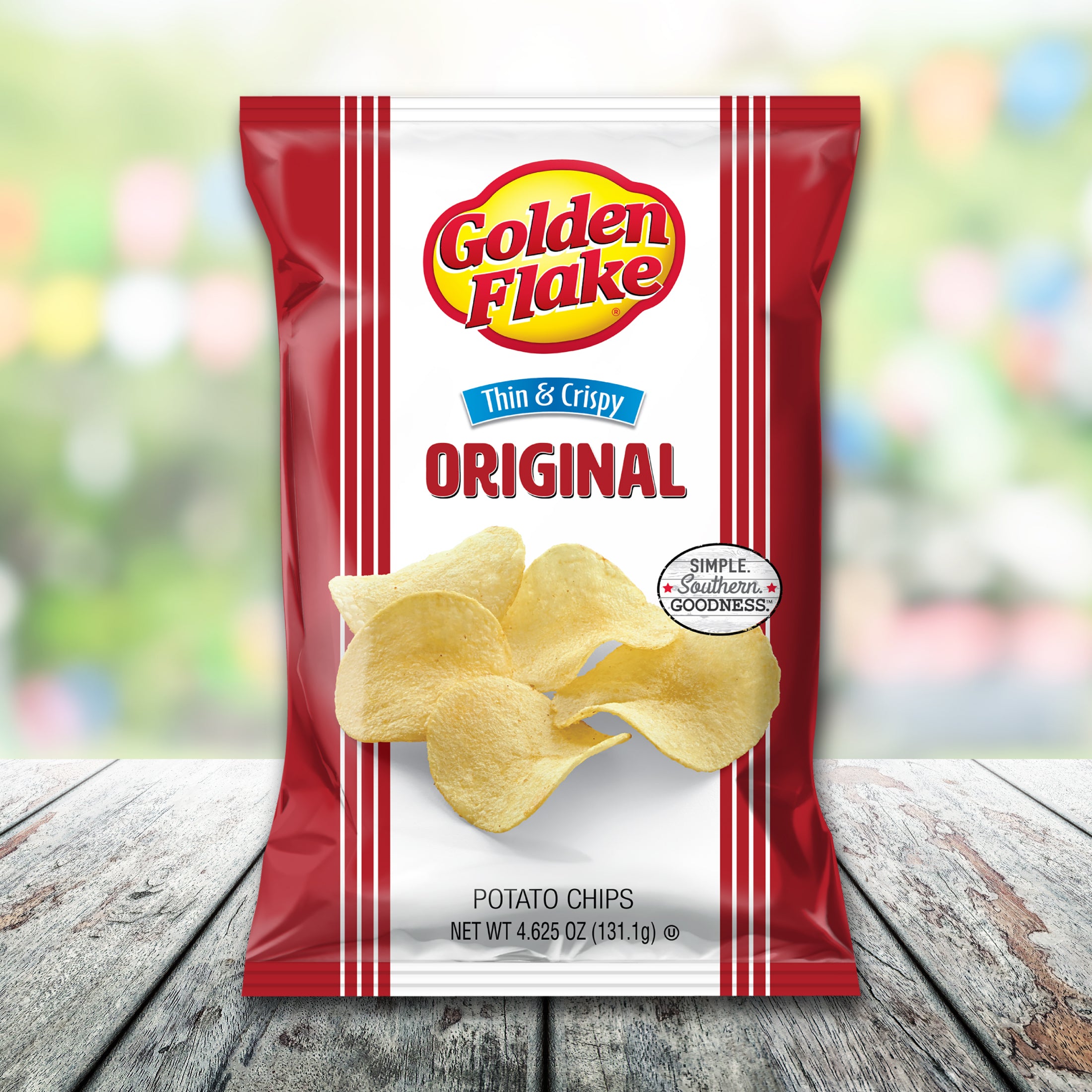 Packaging of Golden Flake Original thin crispy potato chips on a wooden surface with a blurred colorful background.