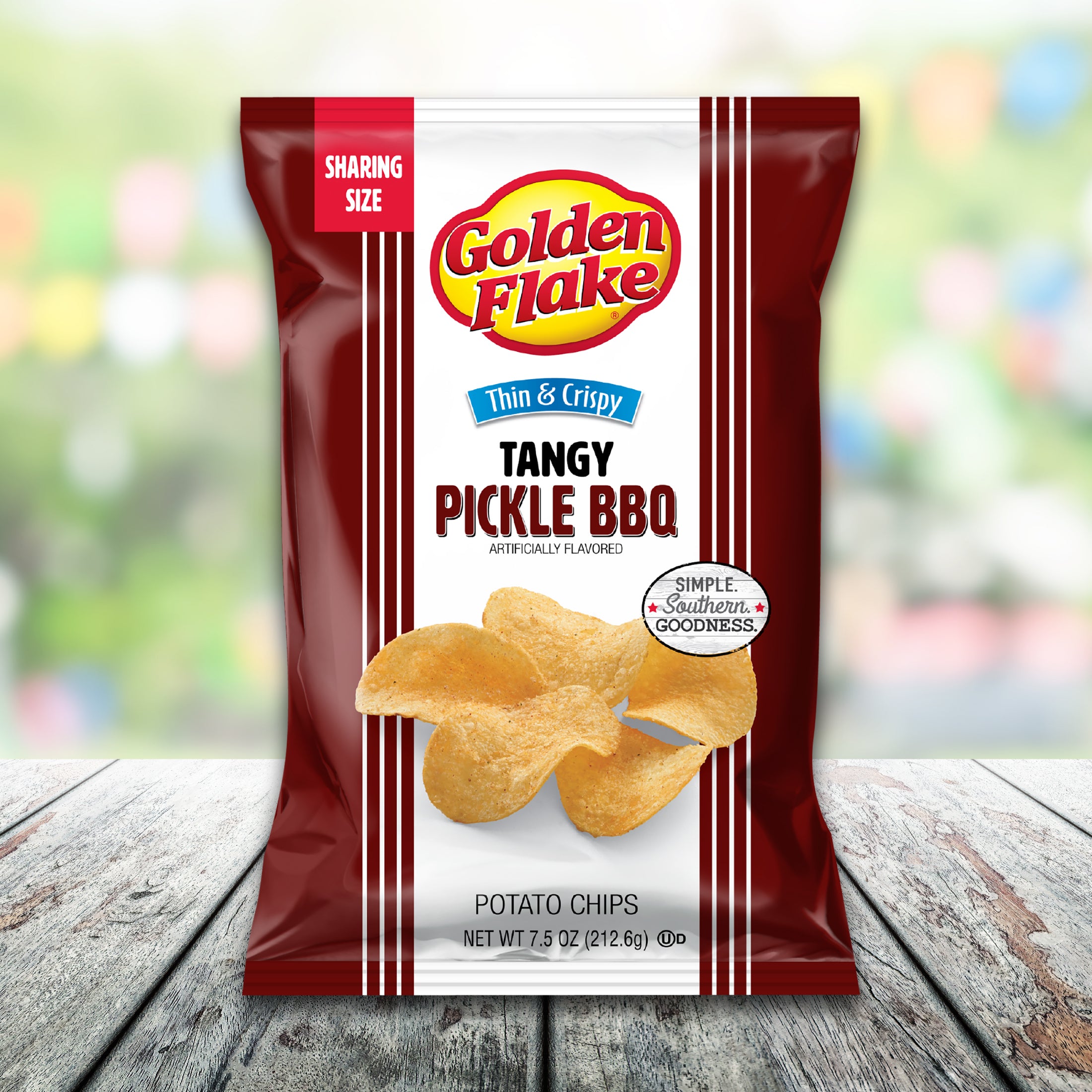 Bag of Golden Flake Tangy Pickle BBQ potato chips on a wooden surface with a blurred colorful background