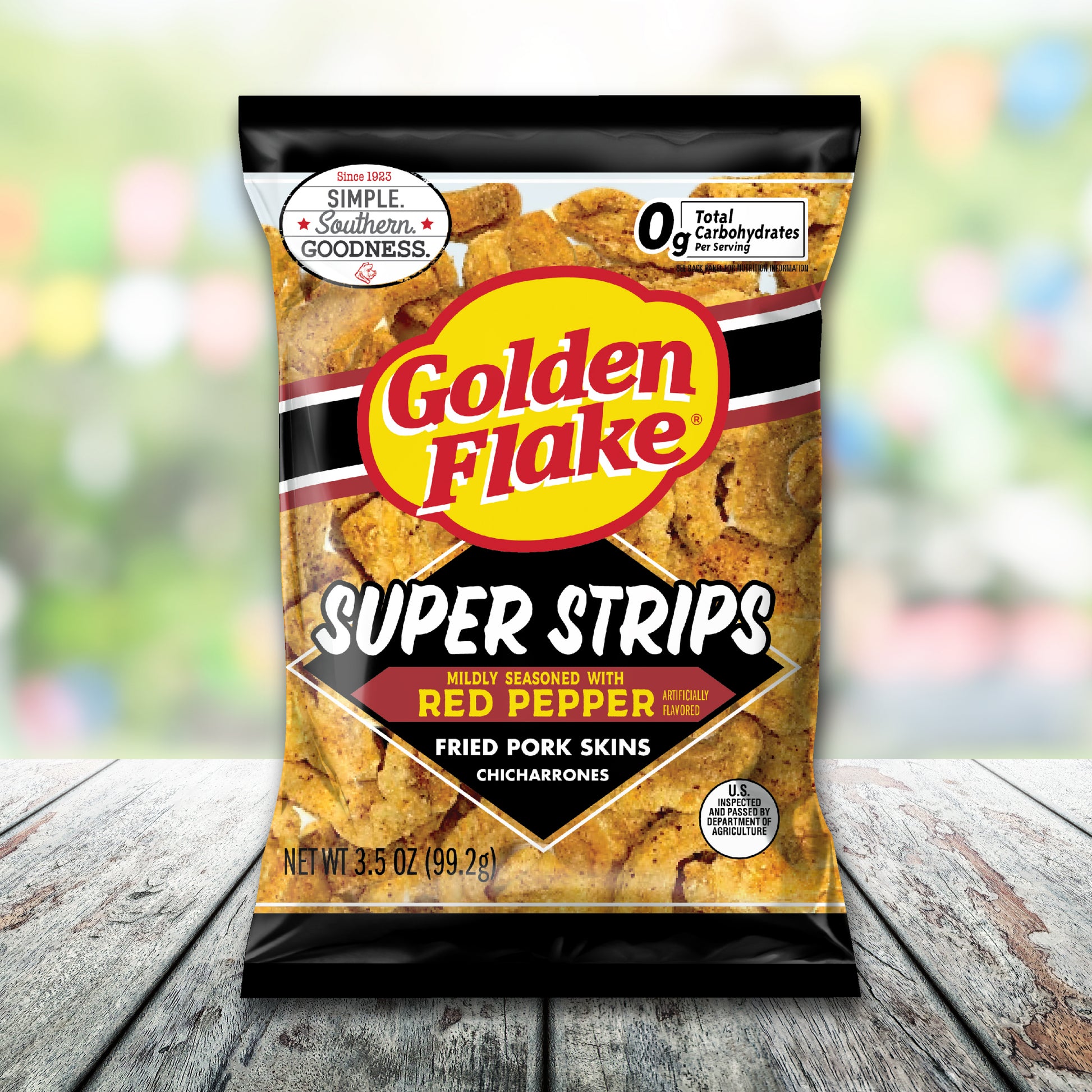Bag of Golden Flake Super Strips fried pork skins on a wooden surface with a blurred colorful background