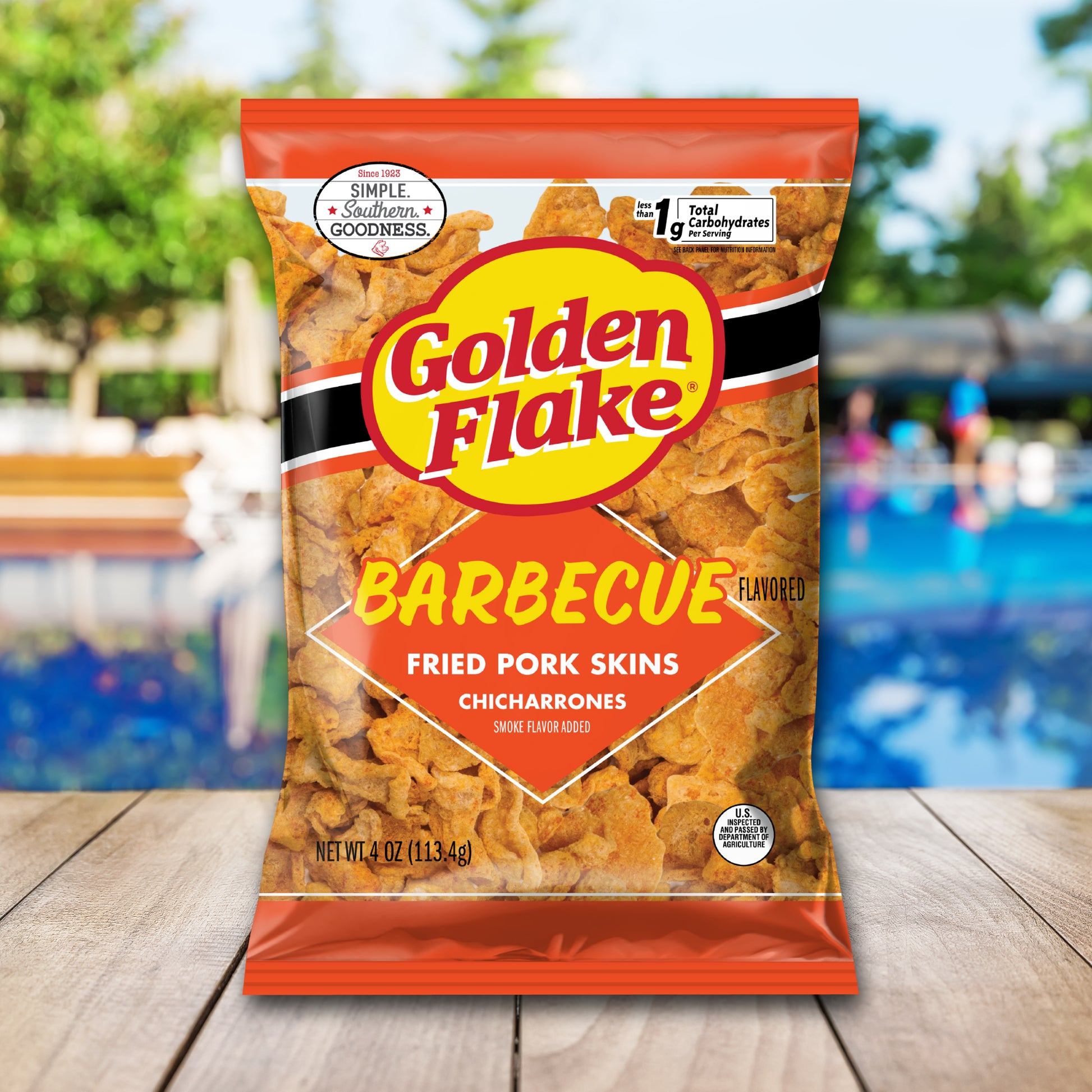 Bag of Golden Flake Barbecue flavored fried pork skins on a wooden surface with a blurred outdoor background.