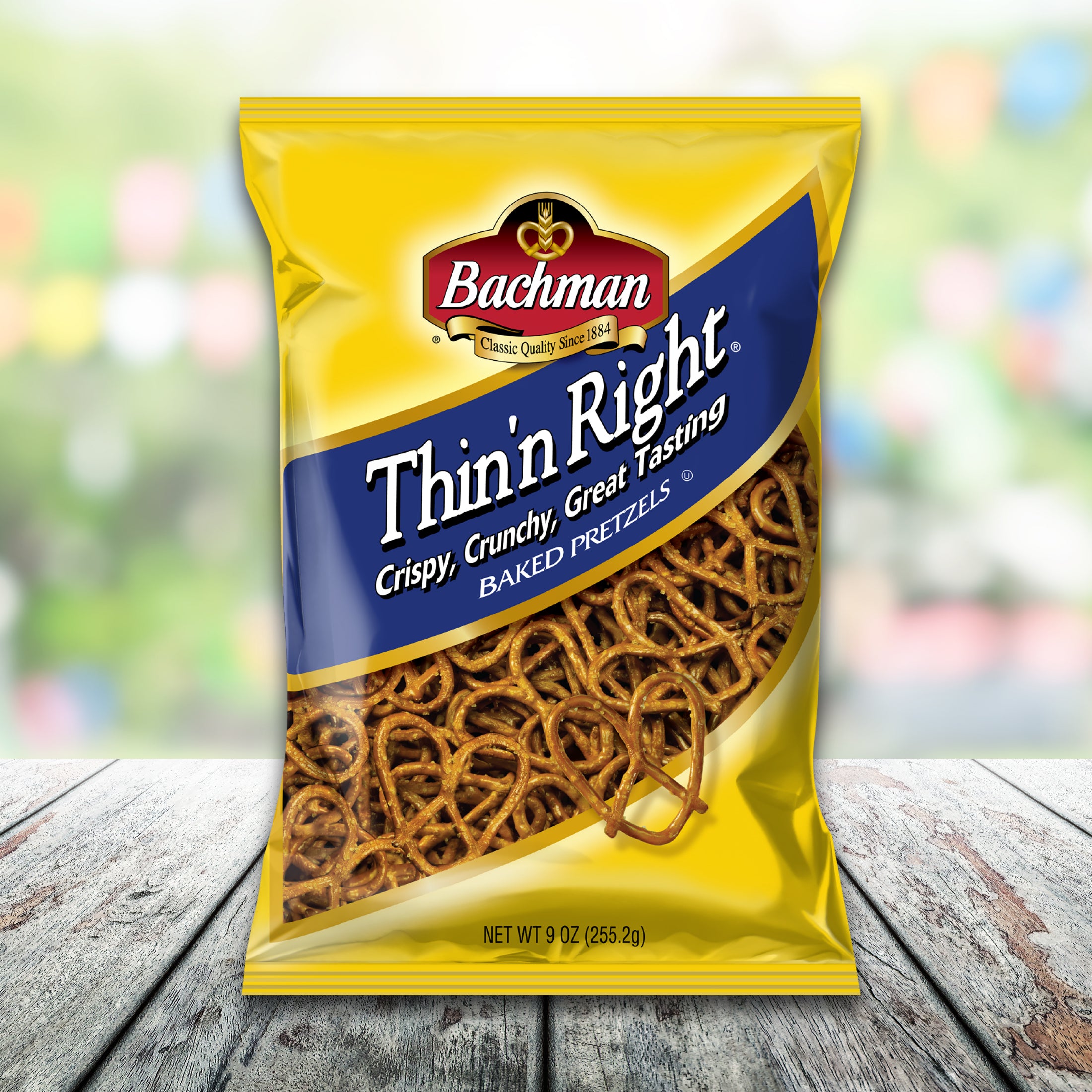Packaged snack of Bachman Thin 'n Right Baked Pretzels on a wooden surface with a blurred colorful background.