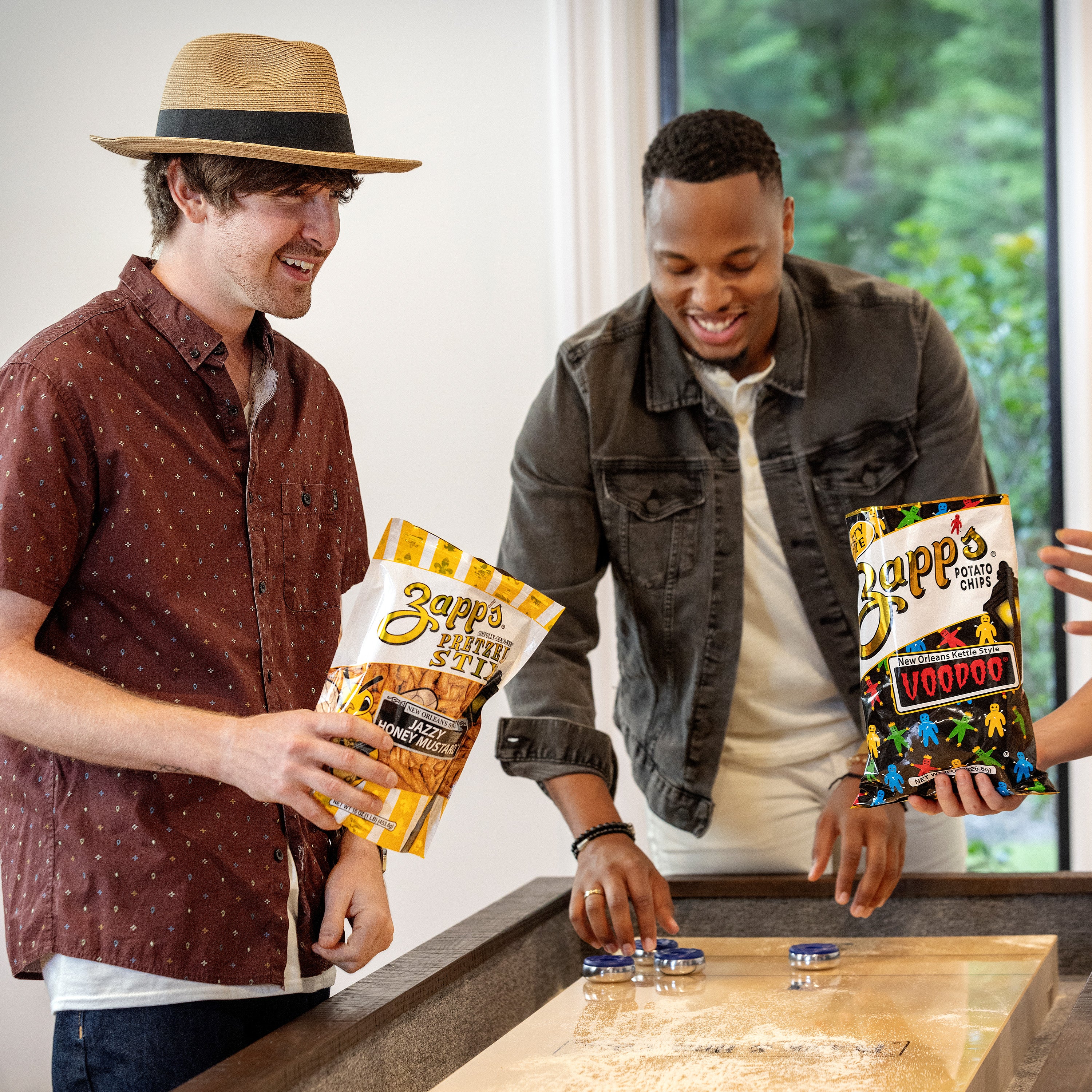 Two men holding Zapp's and Crisps packages in a casual setting.