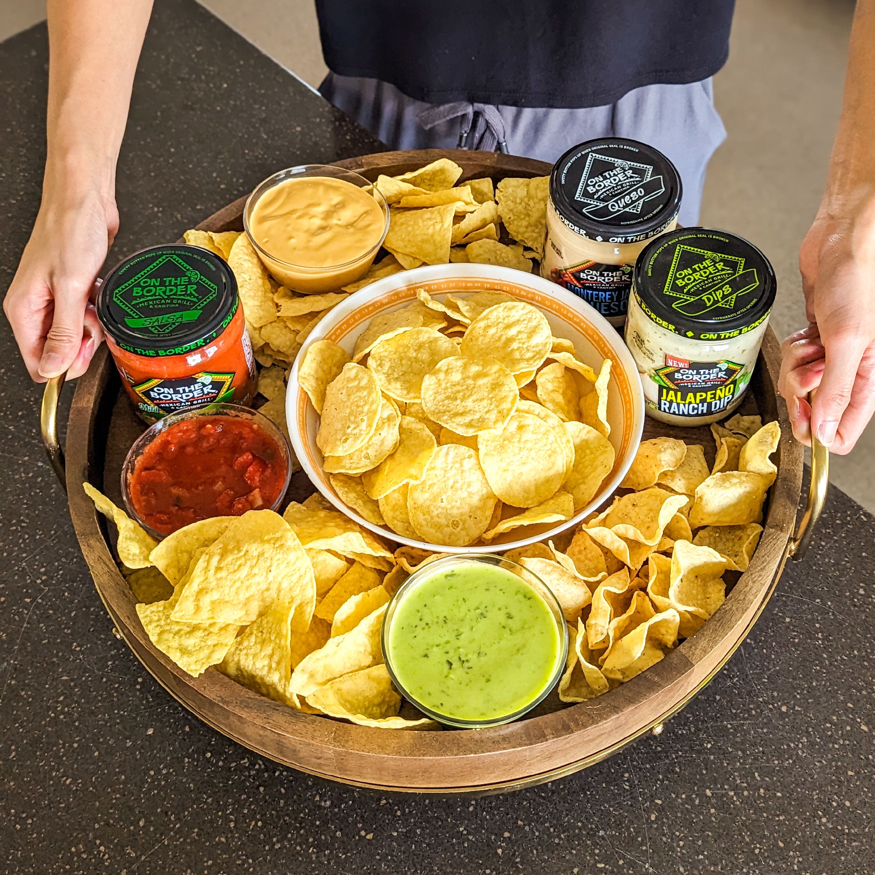 Tray of tortilla chips and salsa with a person holding it on a dark surface