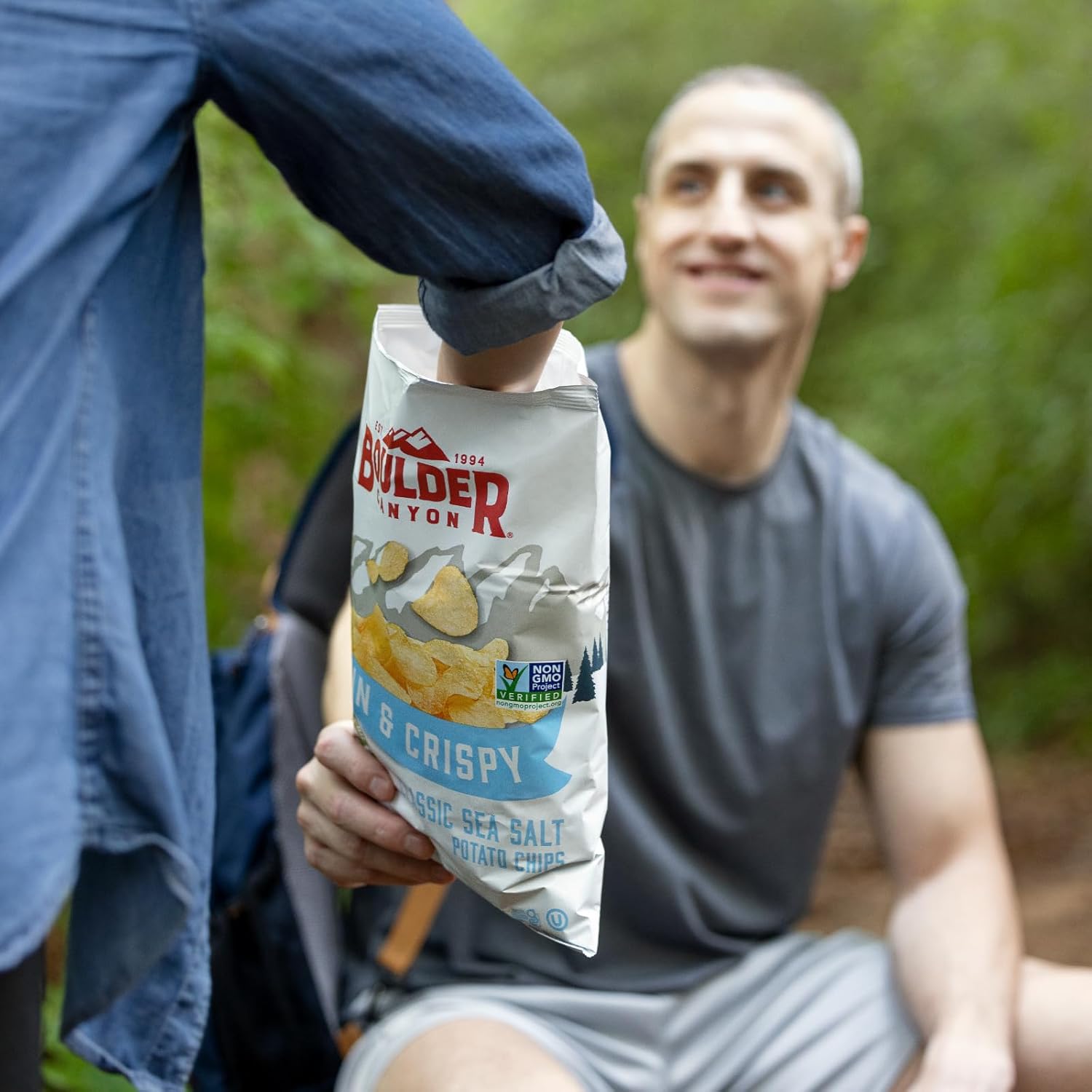 Person holding a bag of Bolden Chips & Crispy Classic Sea Salt potato chips with a man in the background.