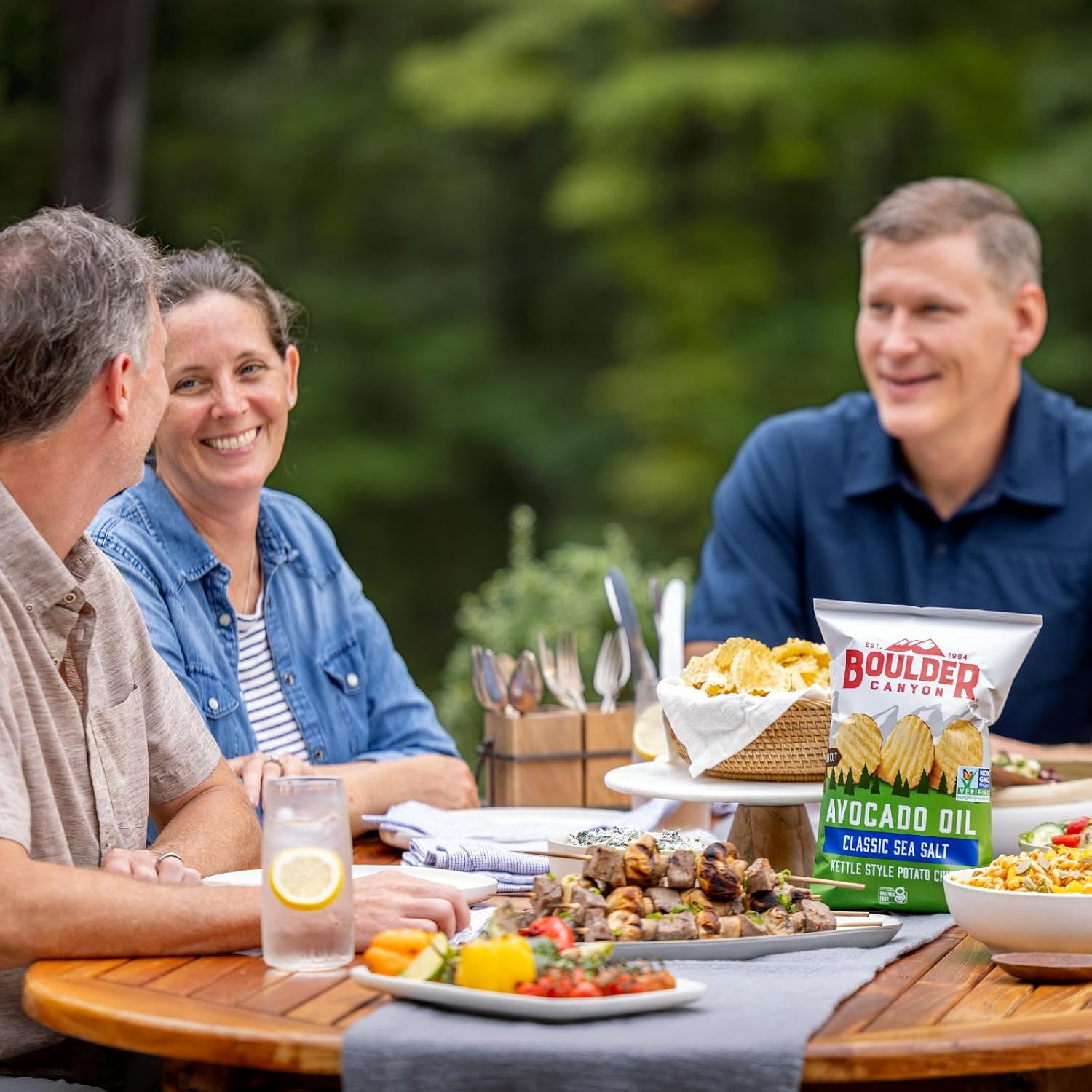 Three people sitting around a table with food and Boulder Canyon chips.