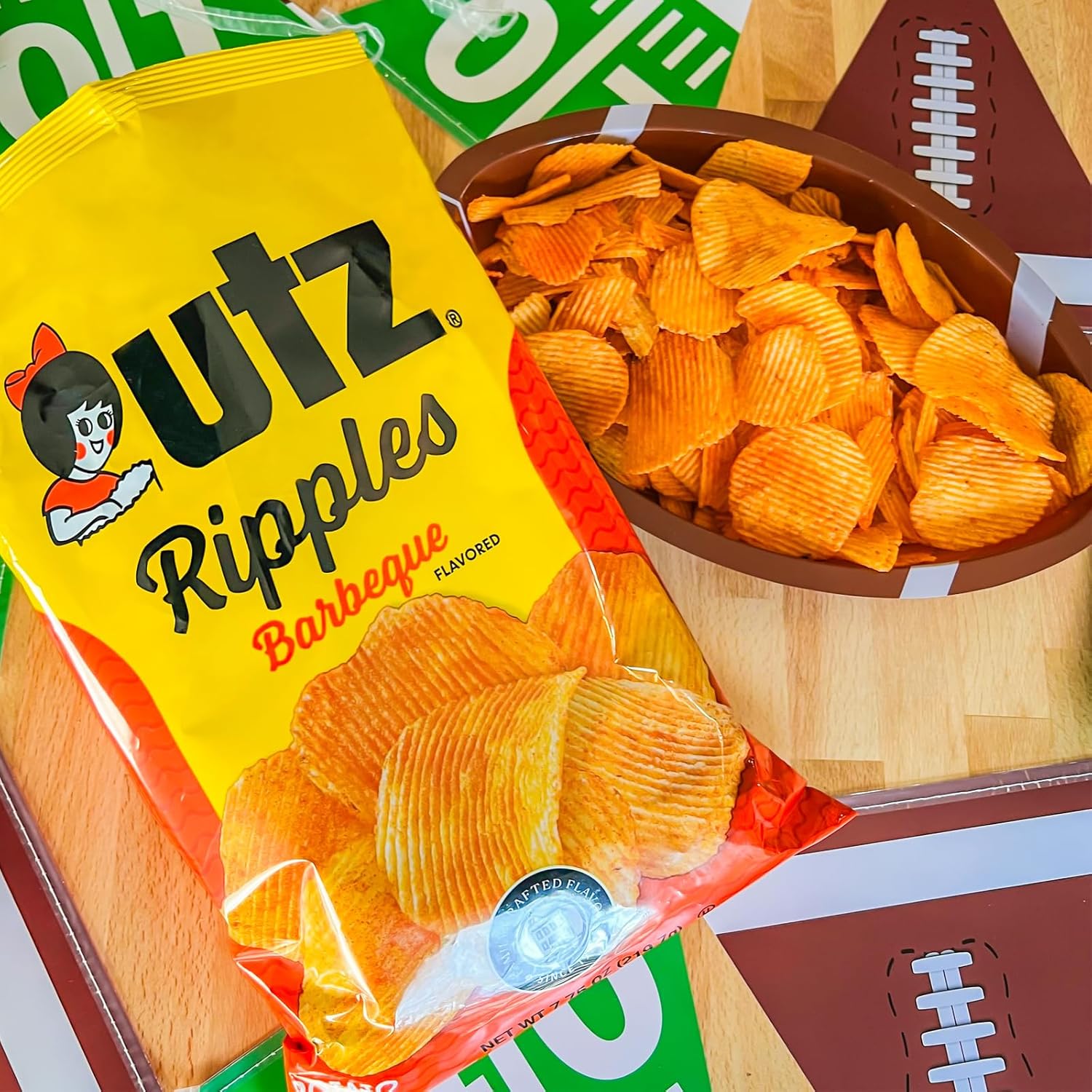 UTZ Ripples Barbeque flavored chips in a yellow bag with a bowl of chips on a sports-themed background.