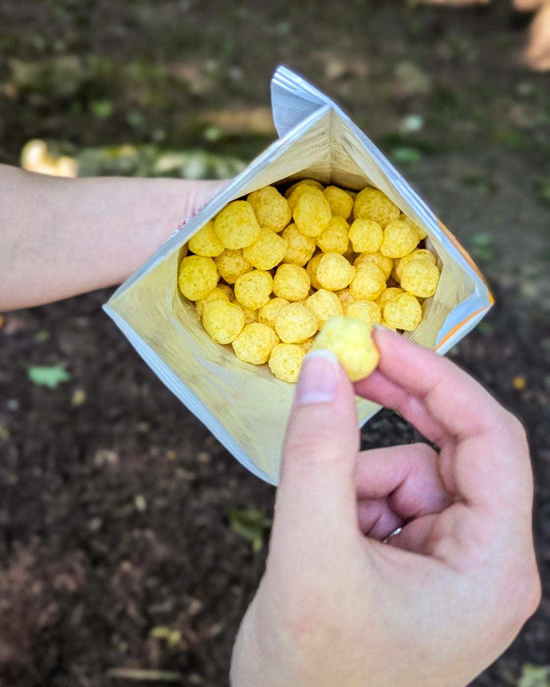 Hand holding a small container of yellow cereal balls outdoors