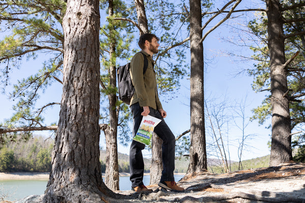Man standing in a forest holding a bag with a visible brand logo.