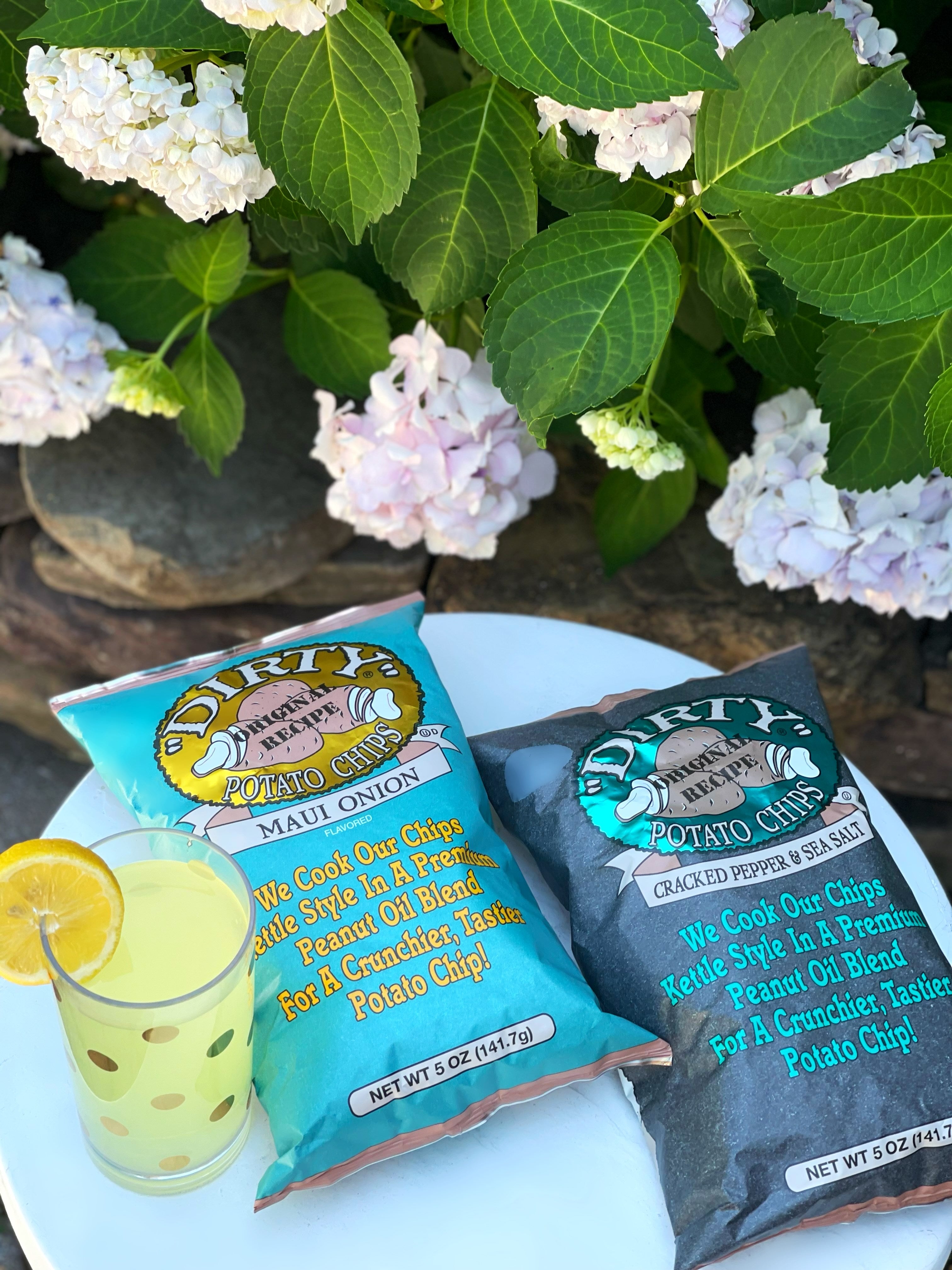 Two bags of Dirty Buddha Chips with a lemonade on a white surface with flowers in the background