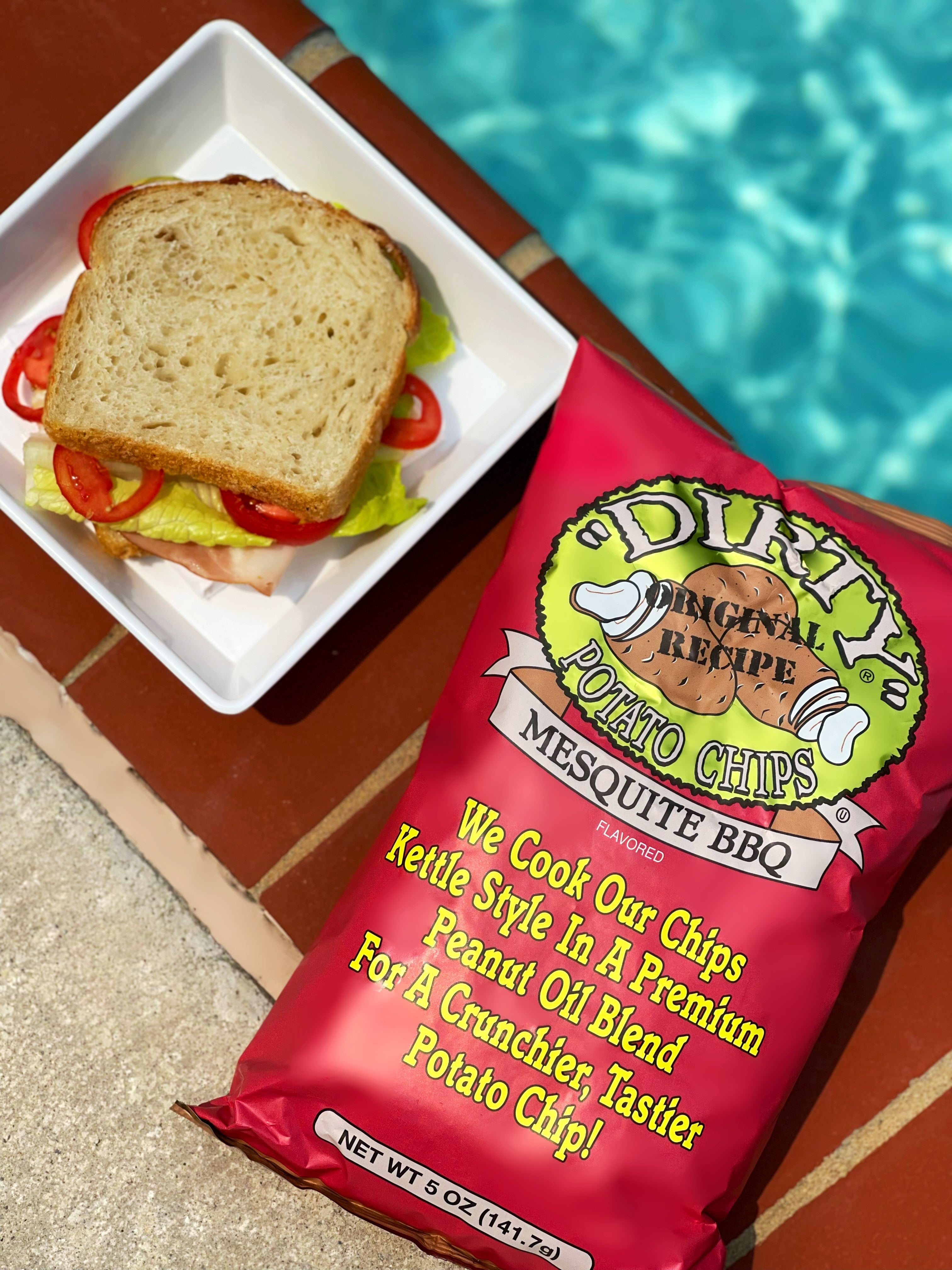 Dirty Original Recipe Mesquite BBQ potato chips next to a sandwich by a pool