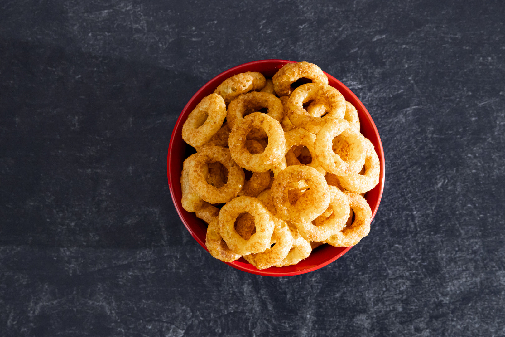 Red bowl filled with round, golden-brown snacks on a dark gray background