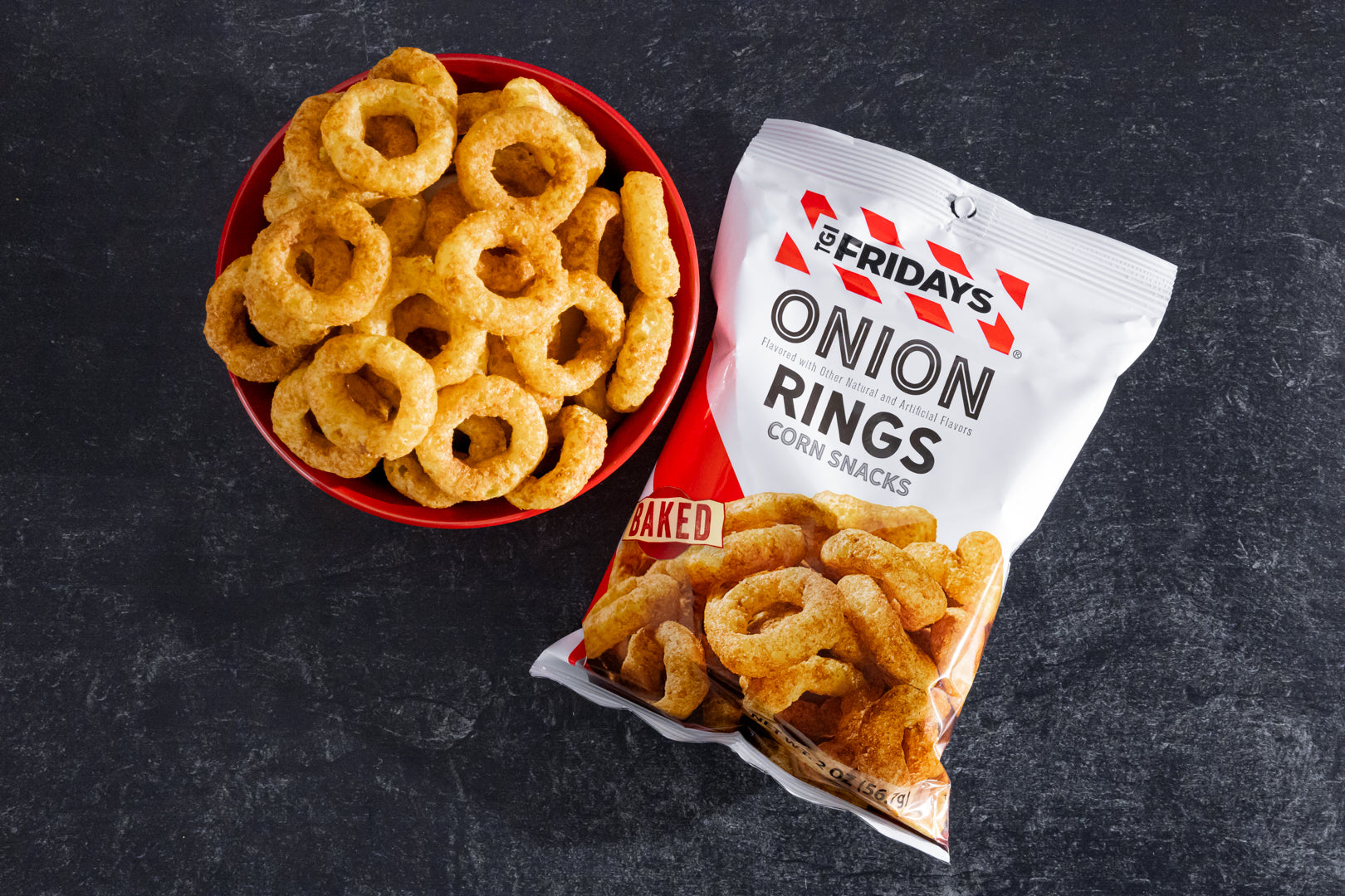 Onion rings in a red bowl and a bag of T.G.I. Friday's onion rings on a dark surface