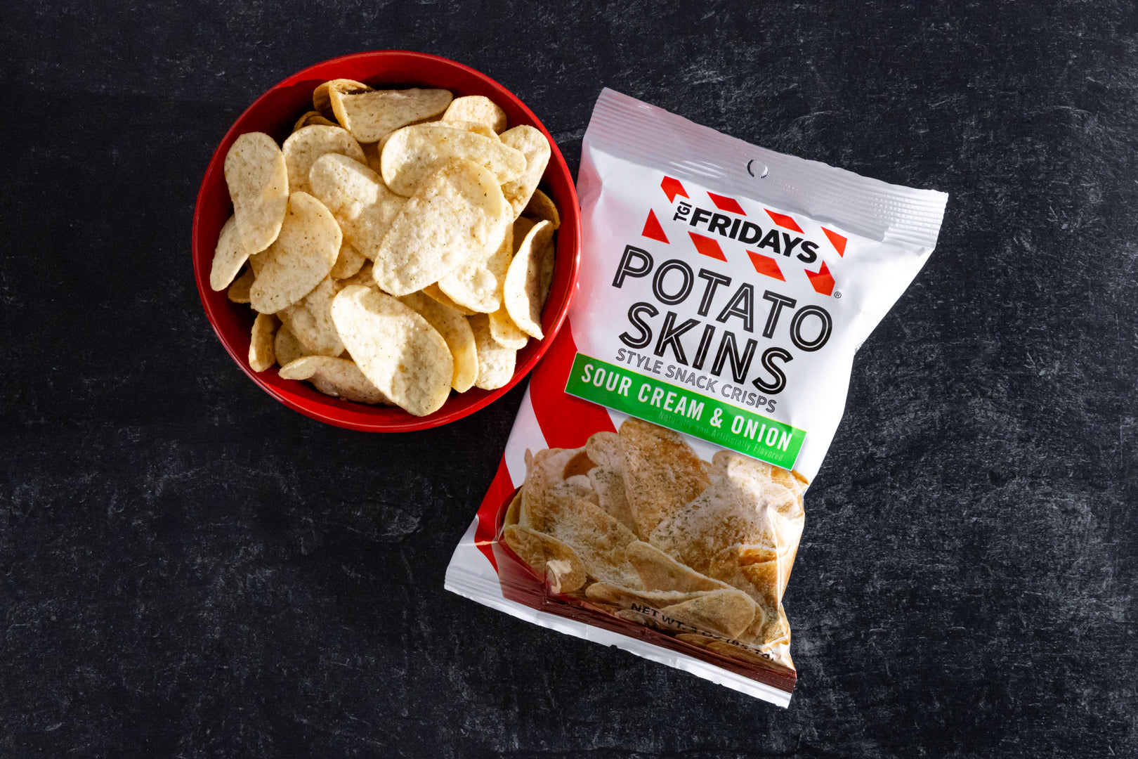 Red bowl of potato skins next to a 'TGI Fridays' package on a dark surface