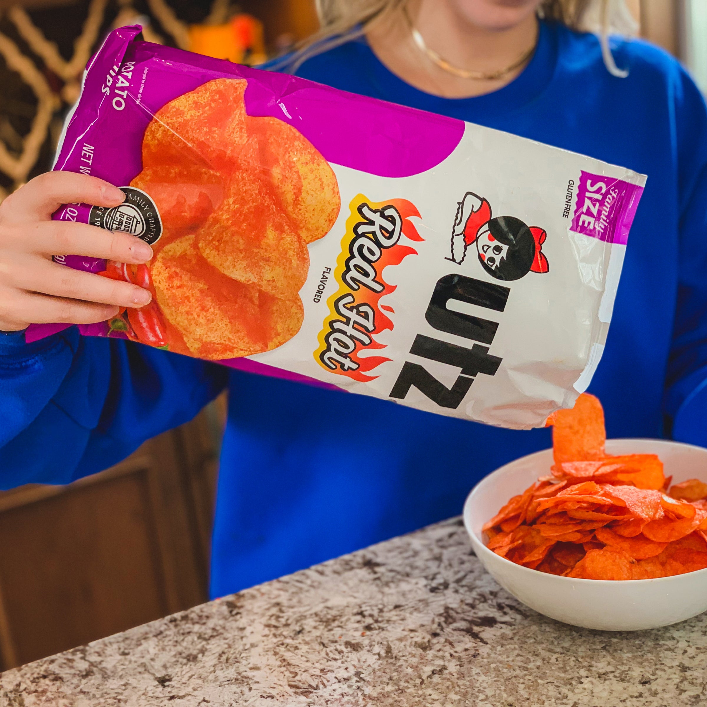 Person holding a bag of Red Hot UZI chips with a bowl of chips on a counter.