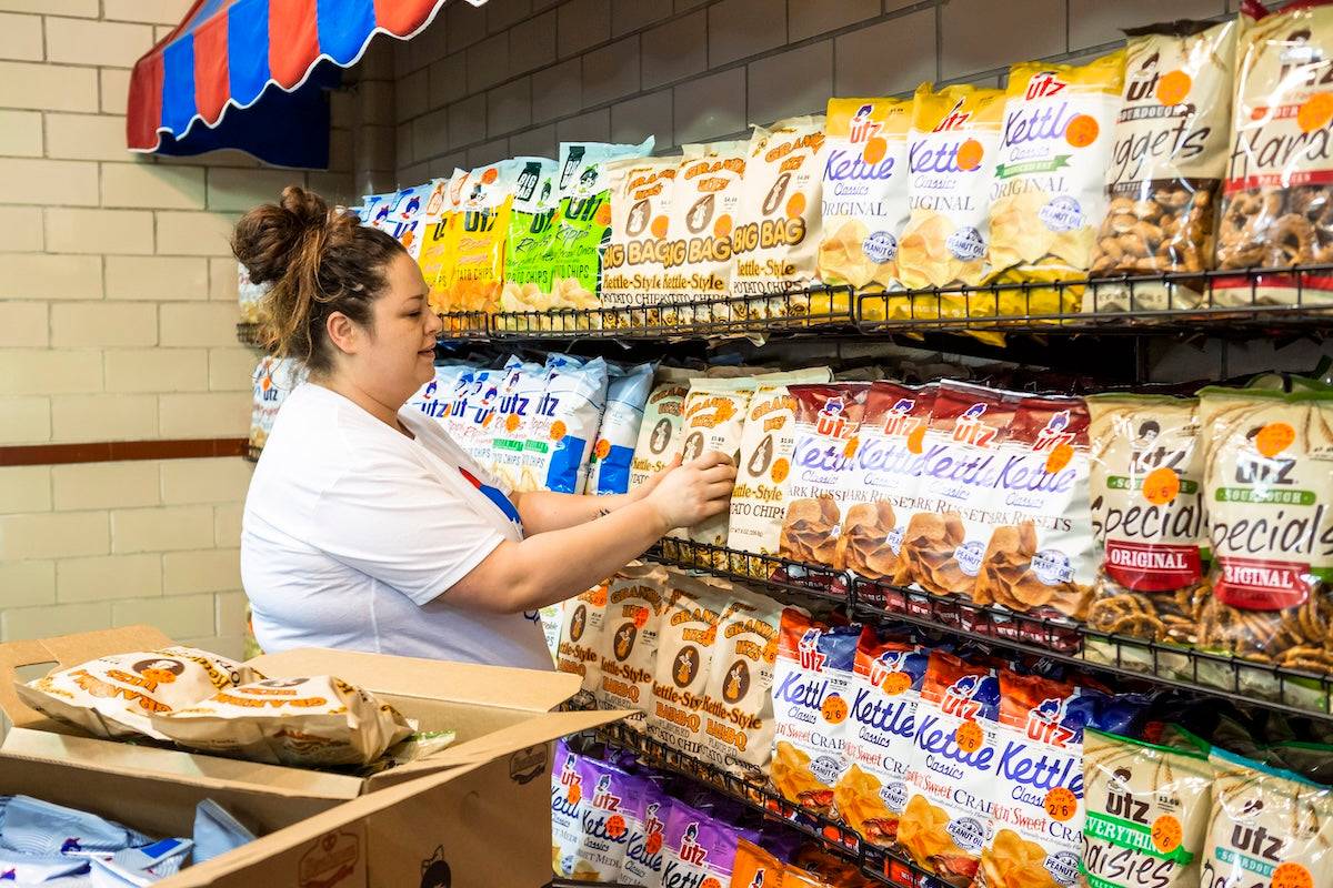Woman shopping at a grocery store with shelves stocked with various snack packages.