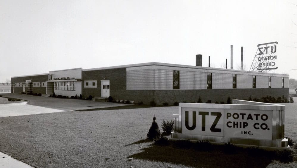 Black and white photograph of a UTZ Potato Chip Co. building with a sign in front.