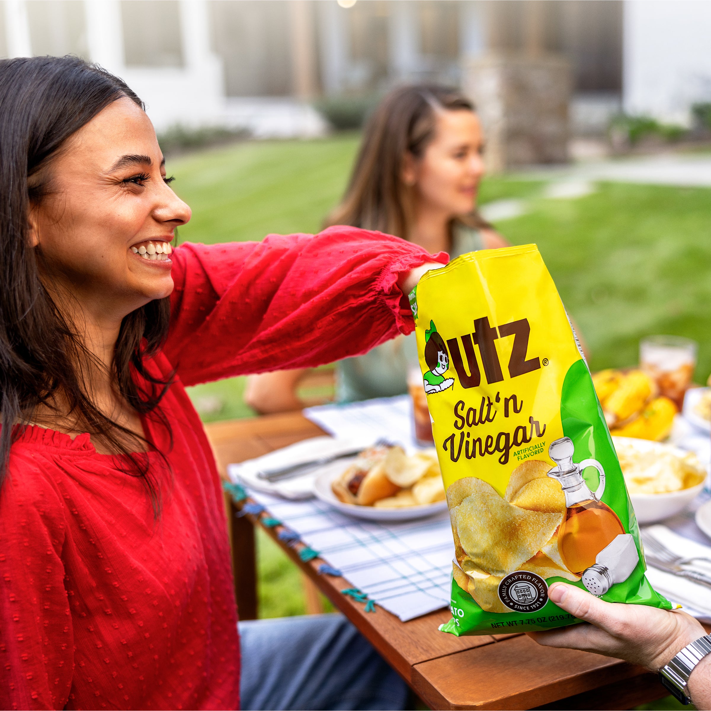 Woman holding a bag of utz Salt 'n Vinegar chips at an outdoor gathering.