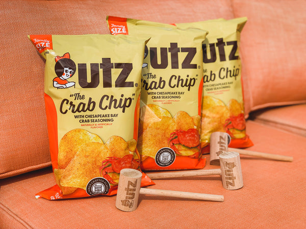 Two bags of Utz The Crab Chip on a pink couch with a small hammer and canister.
