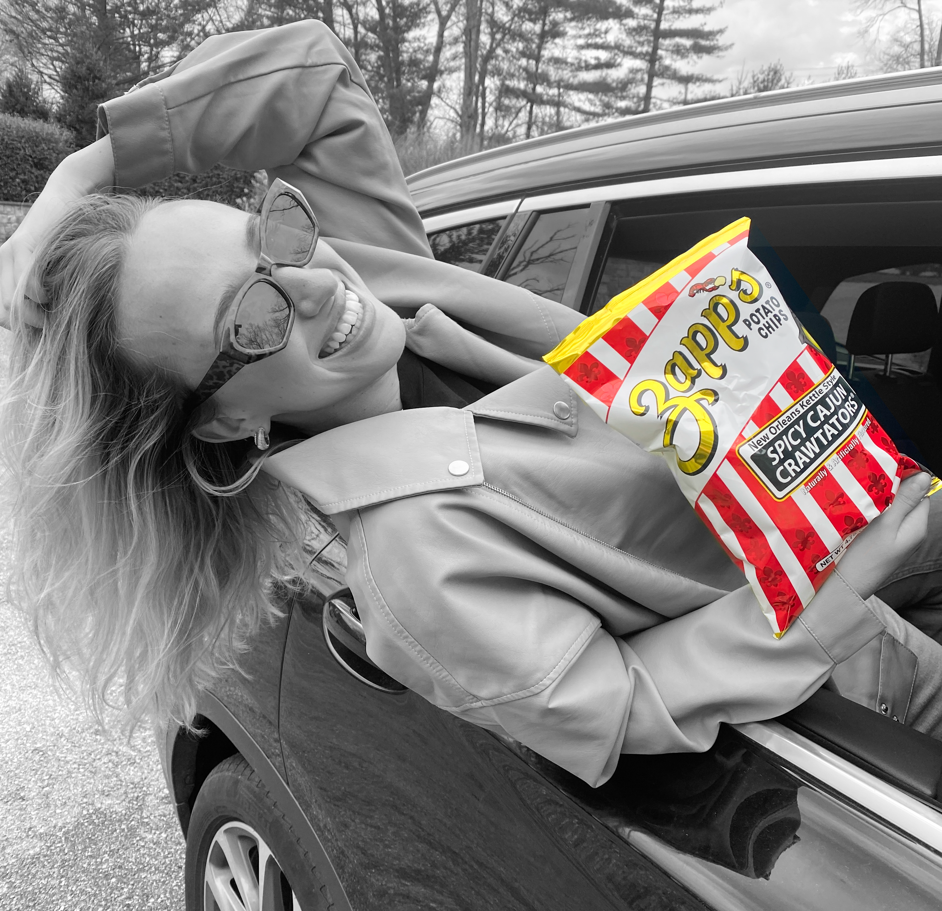 Person leaning out of a car window with a bag of Lay's potato chips.