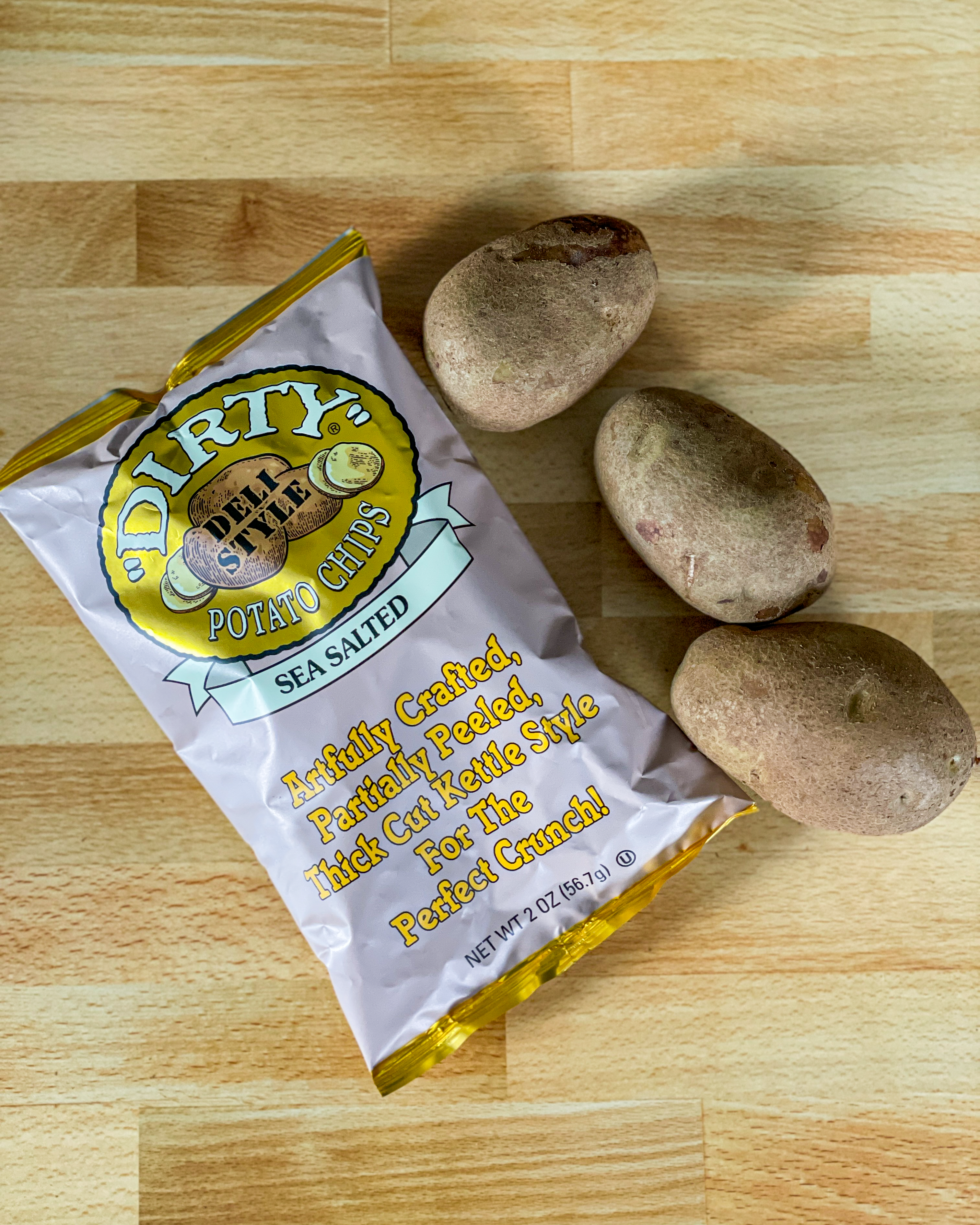 Dirty Potato Chips packaging with three potatoes on a wooden surface